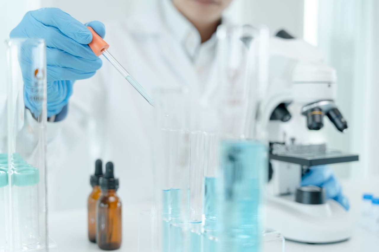 A person in lab coat holding a pipette next to test tubes.